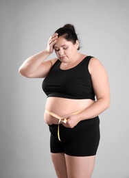 Photo of Fat woman with measuring tape on grey background. Weight loss