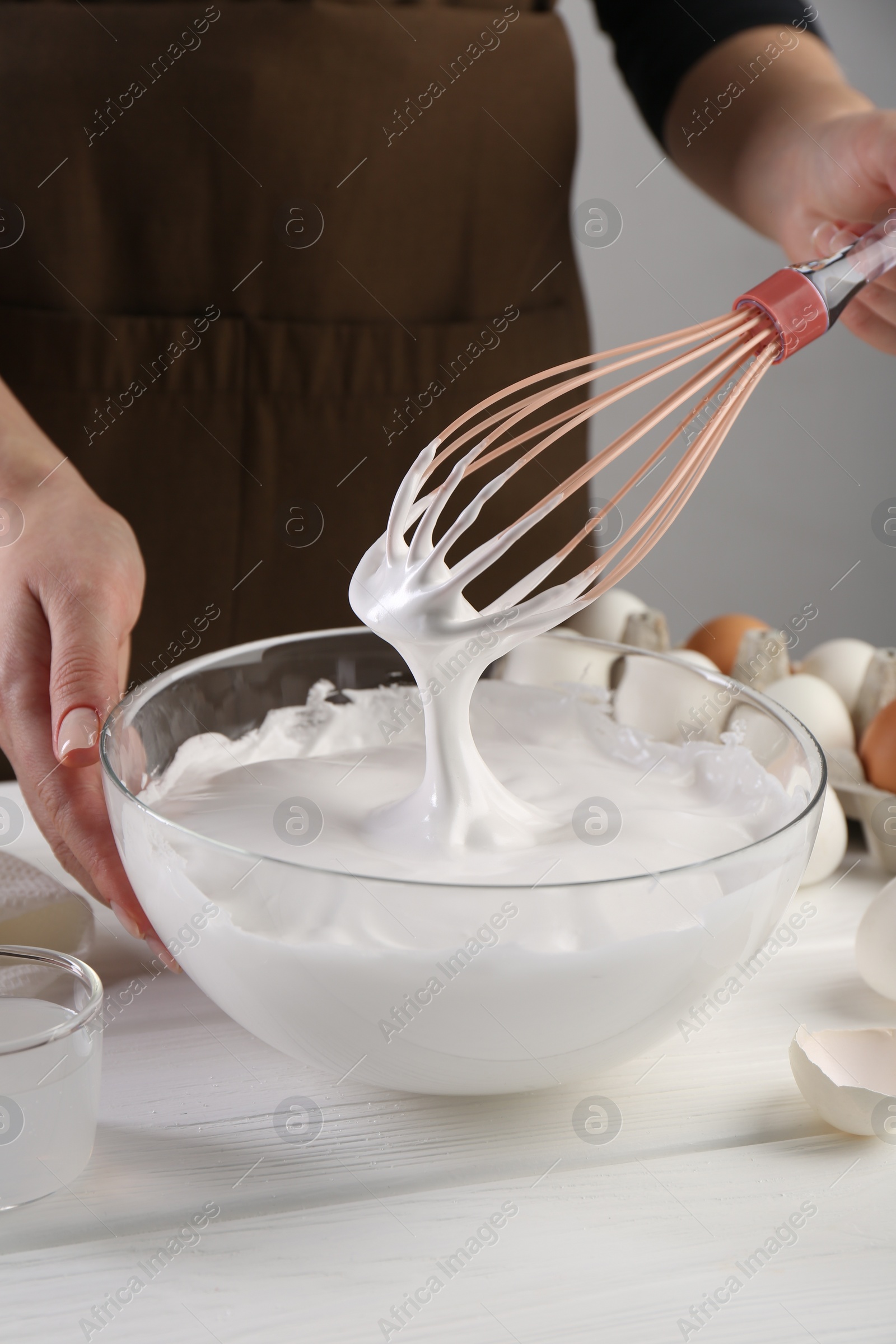 Photo of Woman making whipped cream with whisk at white wooden table, closeup