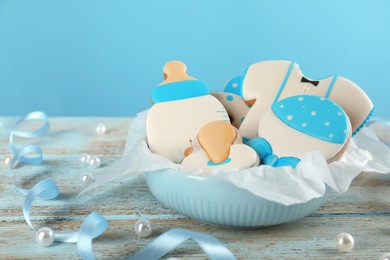 Cute tasty cookies of different shapes, ribbon and scattered pearls on light blue wooden table. Baby shower party
