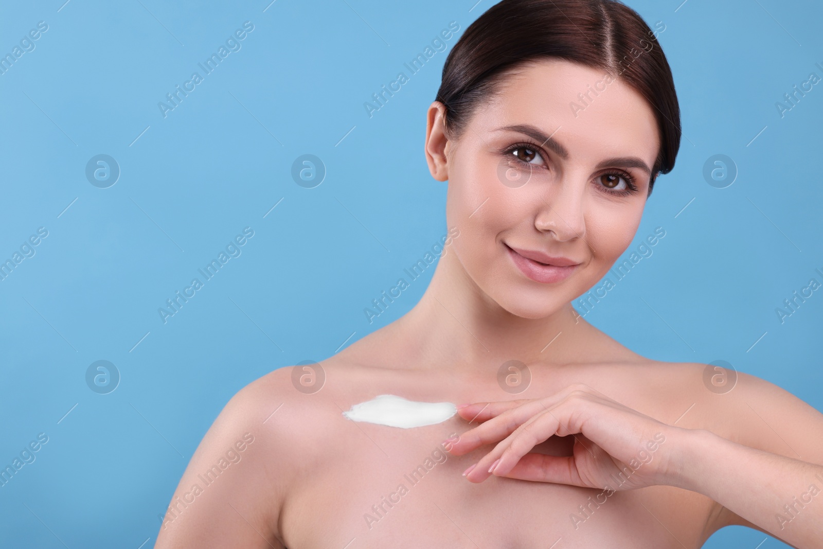 Photo of Beautiful woman with smear of body cream on her collarbone against light blue background, space for text