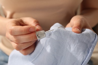 Photo of Woman sewing on light blue fabric with thimble and needle, closeup