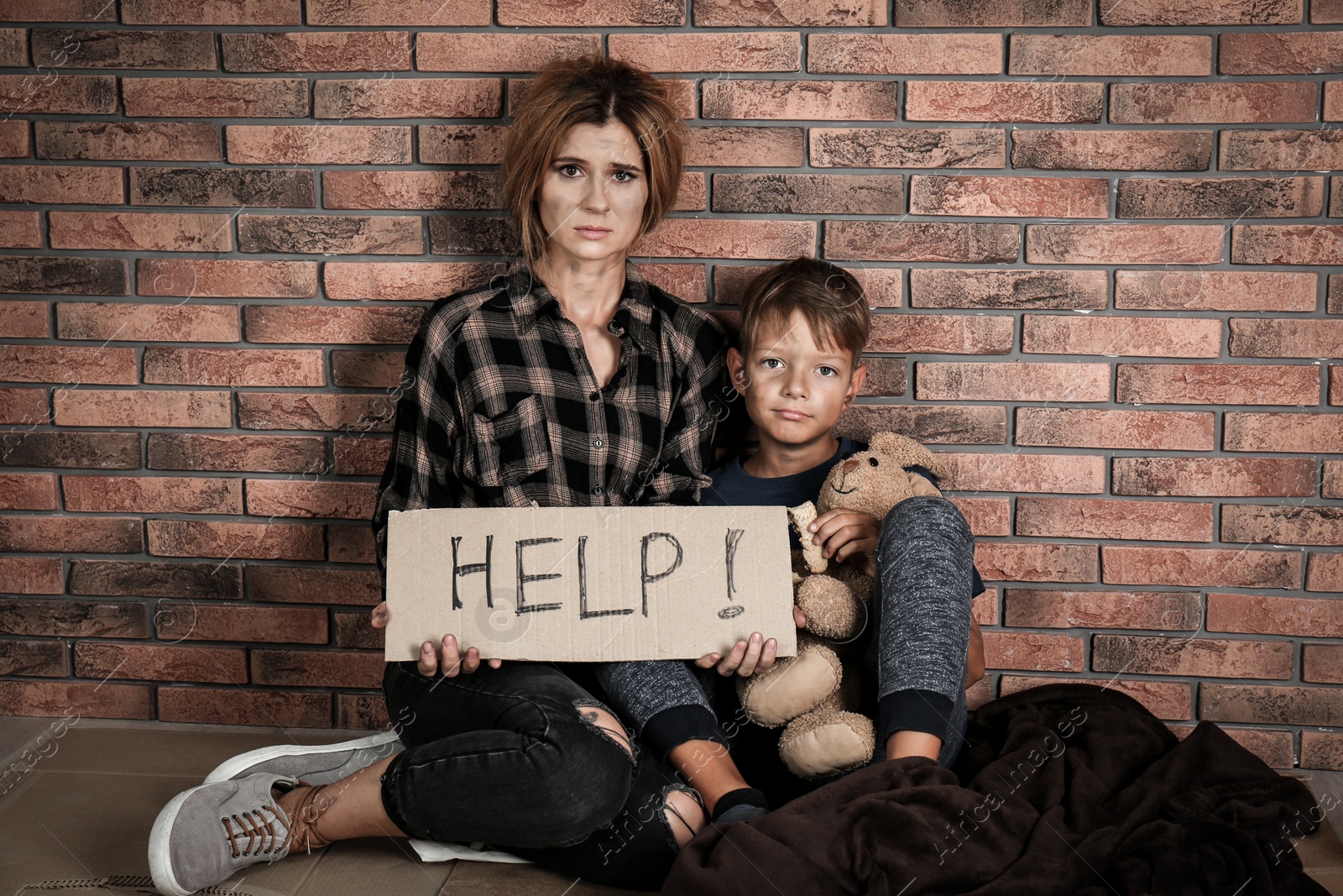 Photo of Poor woman with her son asking for help near brick wall