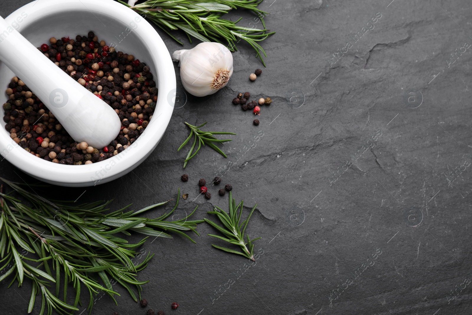 Photo of Sprigs of rosemary, mortar and garlic on black background, flat lay. Space for text