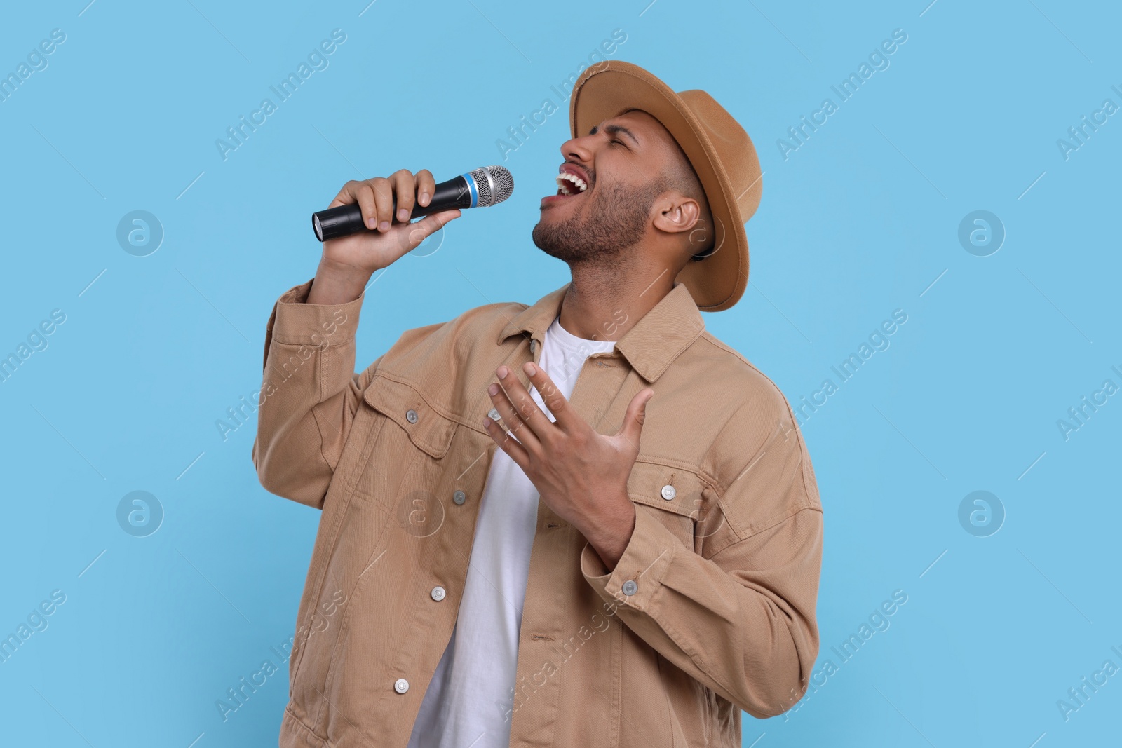 Photo of Handsome man with microphone singing on light blue background