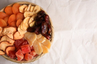 Photo of Wicker basket with different dried fruits on paper, top view. Space for text