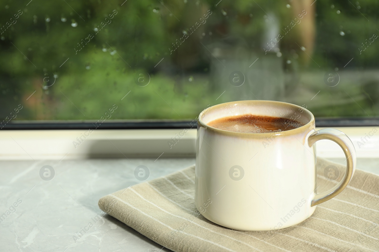 Photo of Cup of hot drink on window sill against glass with rain drops, space for text