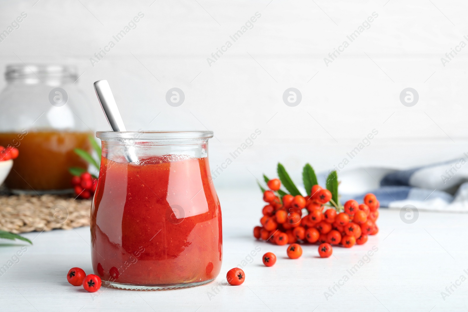 Photo of Delicious rowan jam in glass jar on white wooden table. Space for text