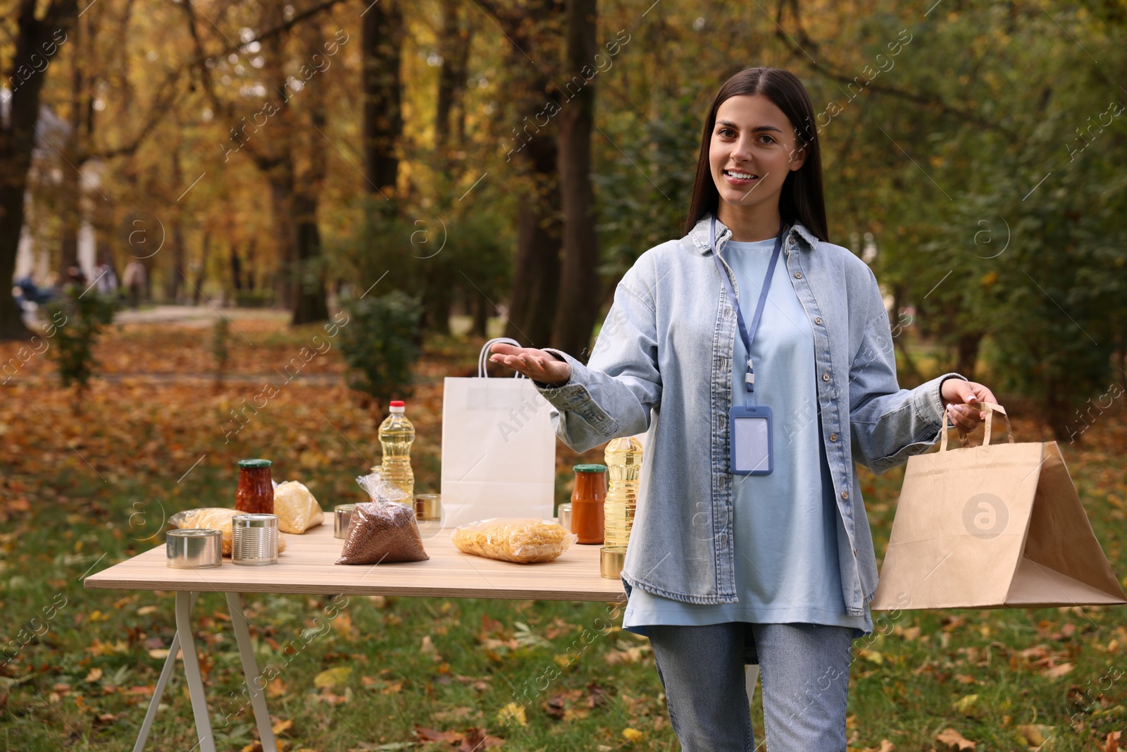 Photo of Portrait of volunteer with paper bag and food products on table in park