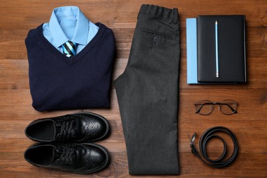 Stylish school uniform for boy, glasses and stationery on wooden background, flat lay