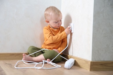 Photo of Little child playing with electrical socket and power strip plug at home. Dangerous situation