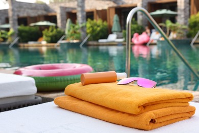 Photo of Beach towels, sunglasses and sunscreen on sun lounger near outdoor swimming pool at luxury resort, selective focus. Space for text