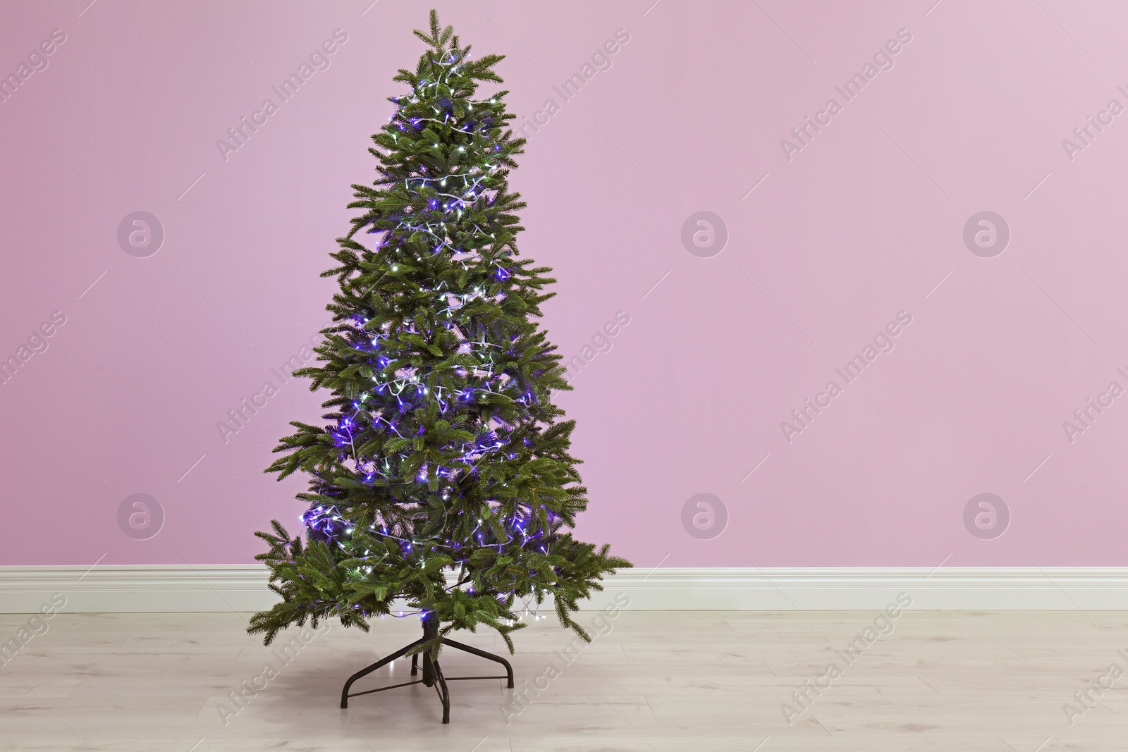 Photo of Beautiful Christmas tree with decor near color wall indoors. Celebration time