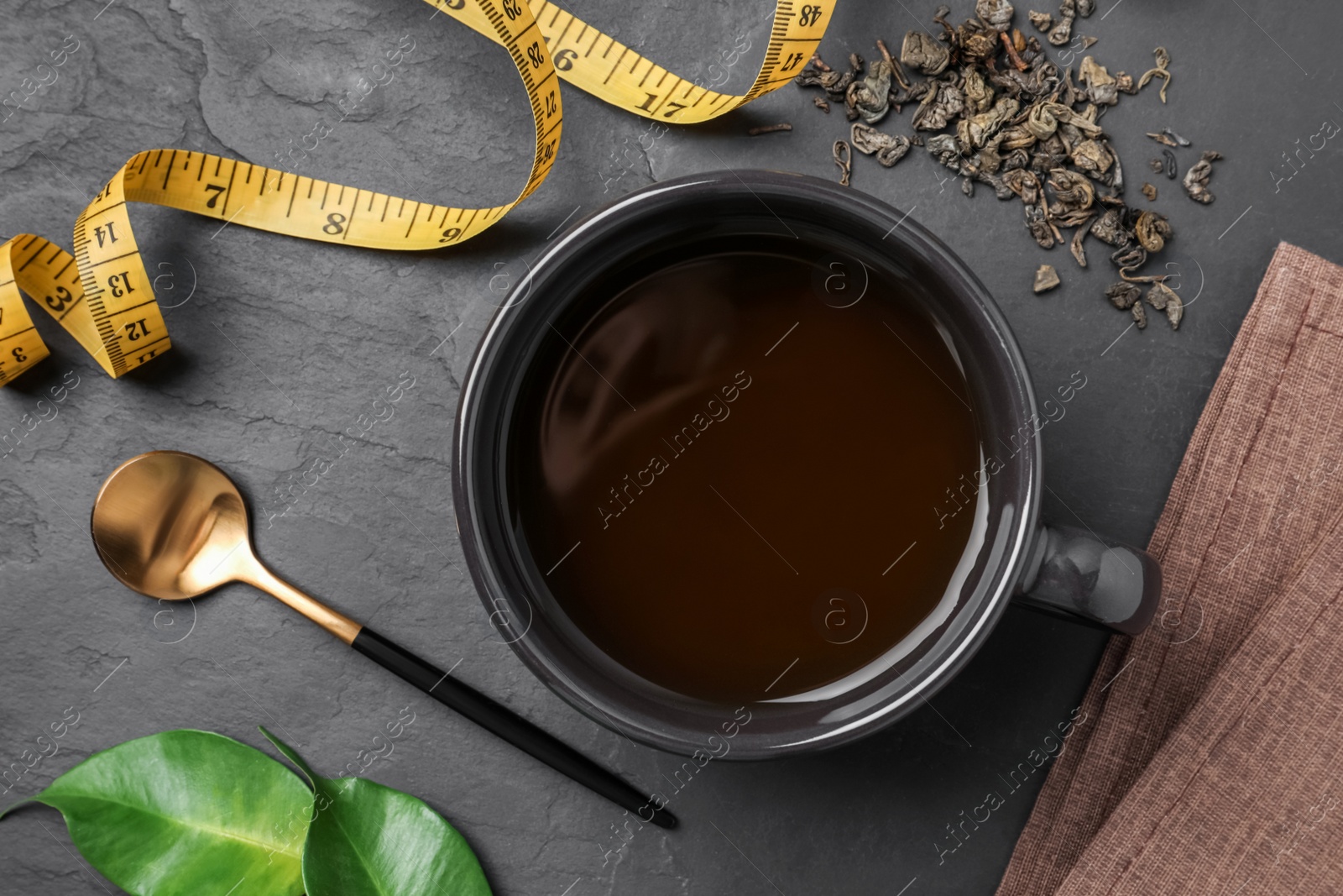 Photo of Cup of herbal diet tea and measuring tape on black table, flat lay. Weight loss concept