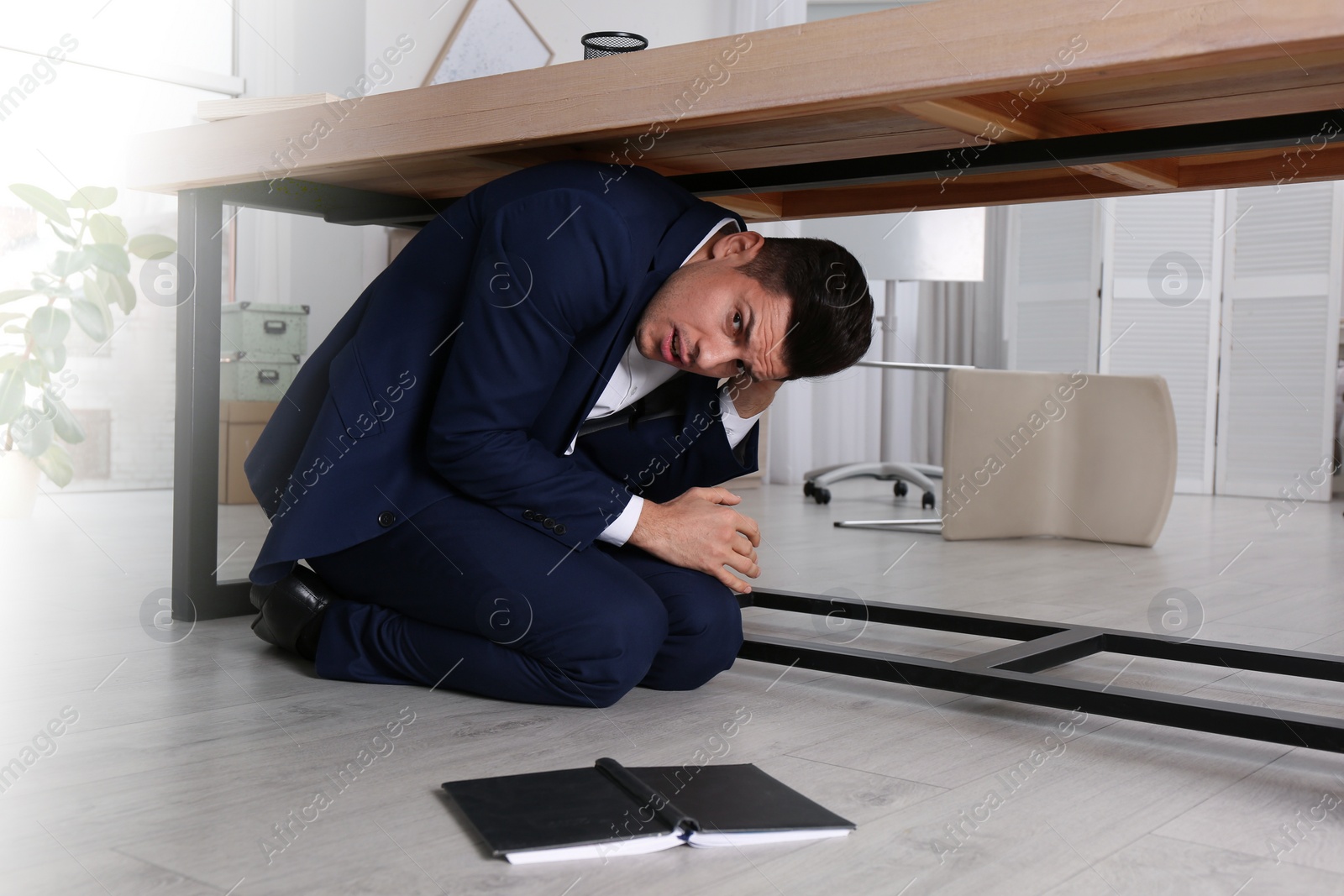 Photo of Scared man hiding under office desk during earthquake