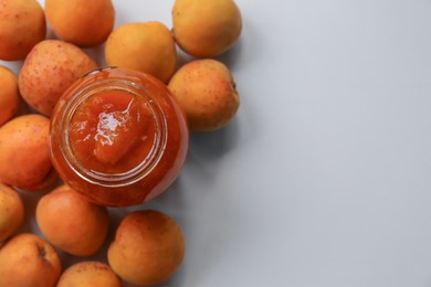 Photo of Jar of delicious jam and fresh ripe apricots on white background, flat lay with space for text. Fruit preserve