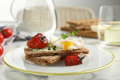 Photo of Fresh rye crispbreads with poached egg, cream cheese and grilled tomatoes on white marble table, closeup