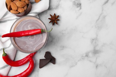 Glass of hot chocolate with chili pepper, anise star and almonds on white marble table, flat lay. Space for text