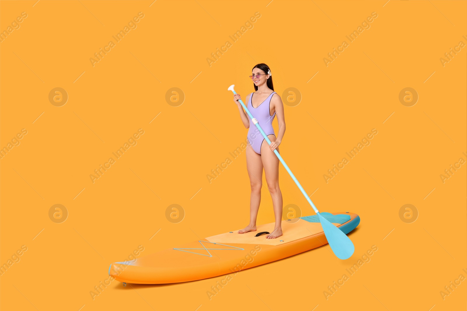 Photo of Happy woman with paddle on SUP board against orange background