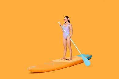 Photo of Happy woman with paddle on SUP board against orange background