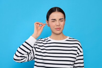 Photo of Young woman cleaning ear with cotton swab on light blue background