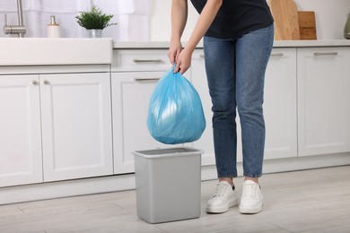 Photo of Woman taking garbage bag out of trash bin in kitchen, closeup