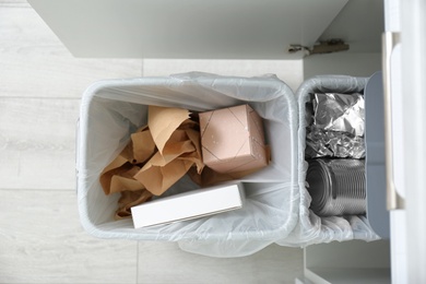 Photo of Open cabinet with full trash bins for separate waste collection in kitchen, top view