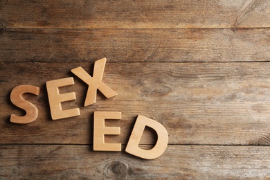 Photo of Phrase "SEX ED" made of different letters on wooden background, flat lay