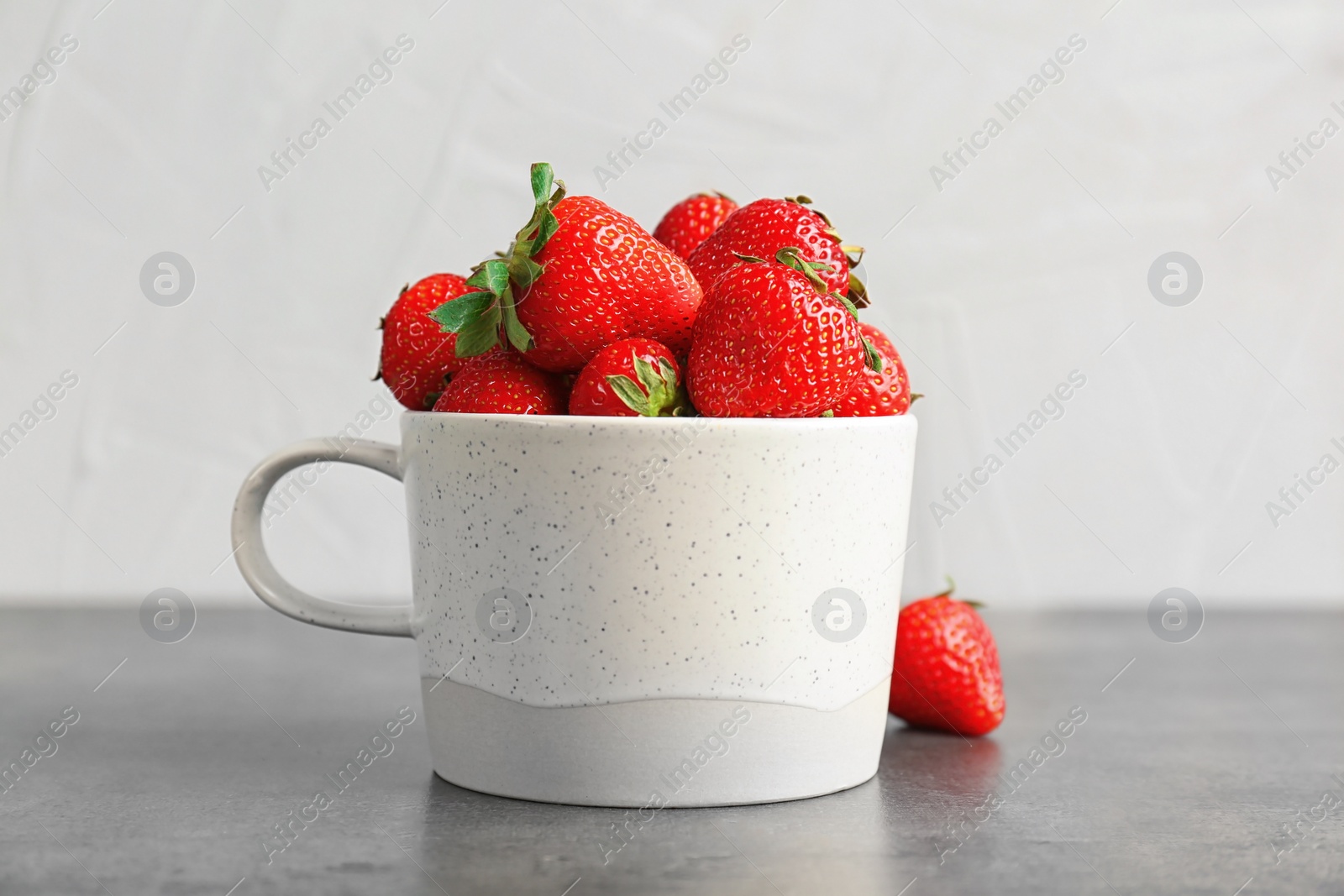 Photo of Mug with ripe red strawberries on table