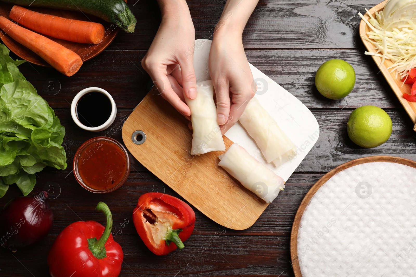 Photo of Woman making delicious spring rolls at wooden table, flat lay