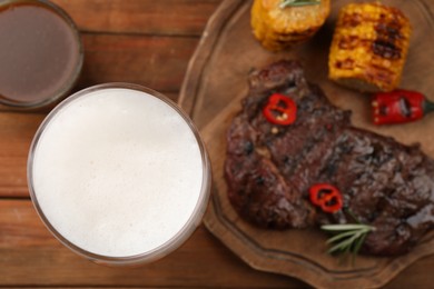 Photo of Glass of beer, delicious fried steak and sauce on wooden table, closeup. Space for text