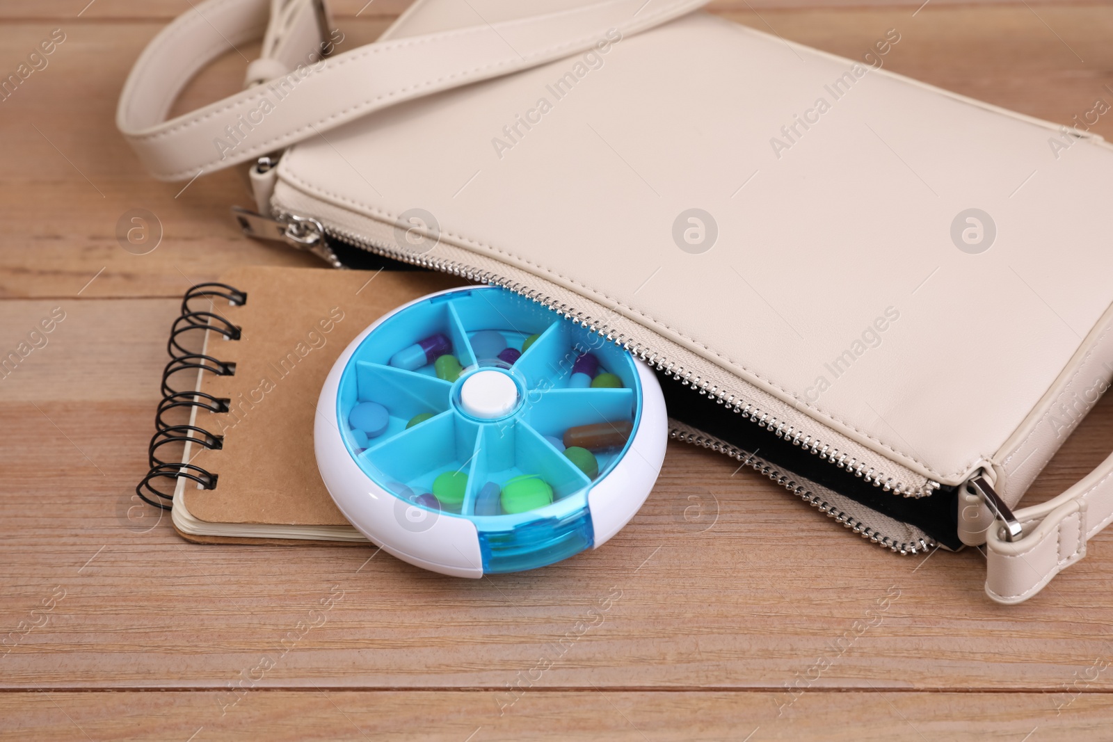 Photo of Stylish women's bag with plastic pill box and notebook on wooden background, closeup