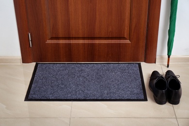 Photo of Welcome mat, male shoes and umbrella at door in hall