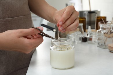 Photo of Woman cutting wick of homemade candle at table indoors, closeup