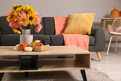 Photo of Beautiful autumn bouquet and small pumpkins on wooden table near sofa in room