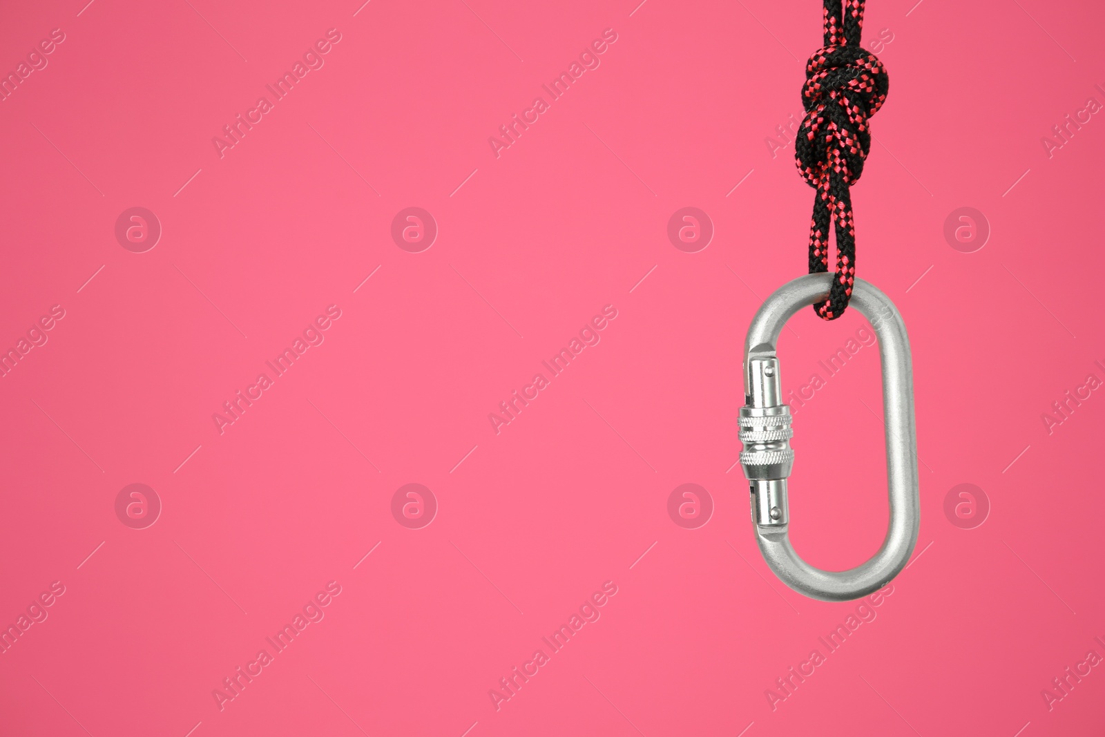 Photo of One metal carabiner hanging on rope against bright pink background. Space for text