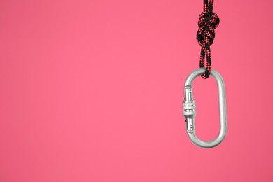 One metal carabiner hanging on rope against bright pink background. Space for text