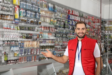 Photo of Salesman standing near showcase with fishing equipment in sports shop. Space for text