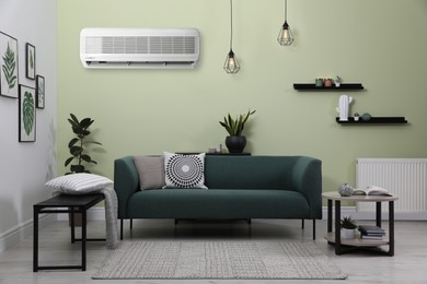 Image of Modern air conditioner on light green wall in living room with stylish furniture