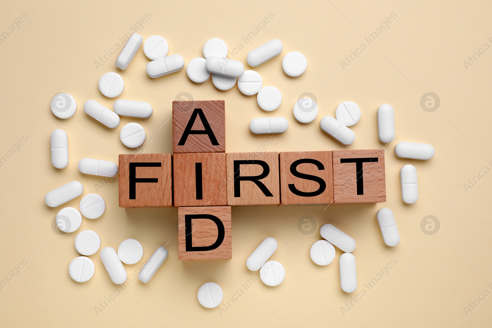Photo of Words First Aid made of wooden cubes and pills on beige background, flat lay