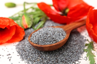 Photo of Spoon of poppy seeds and flowers on white table, closeup