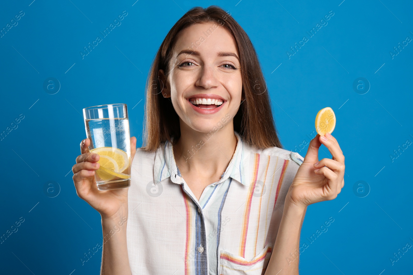 Photo of Young woman with glass of lemon water on light blue background