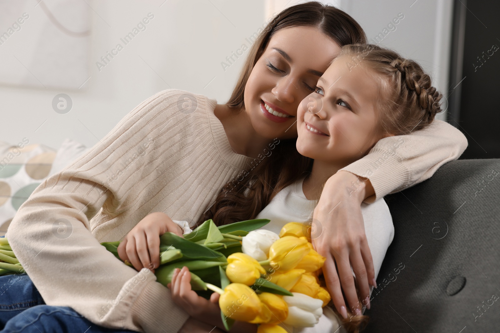 Photo of Happy woman and her cute daughter with bouquet of tulips on sofa at home