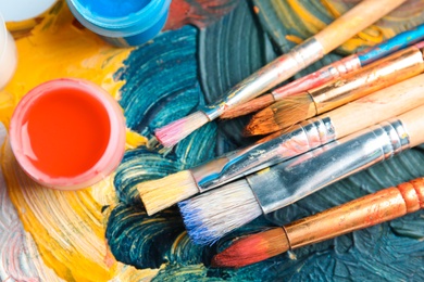 Photo of Different brushes and jars with paint on palette, top view