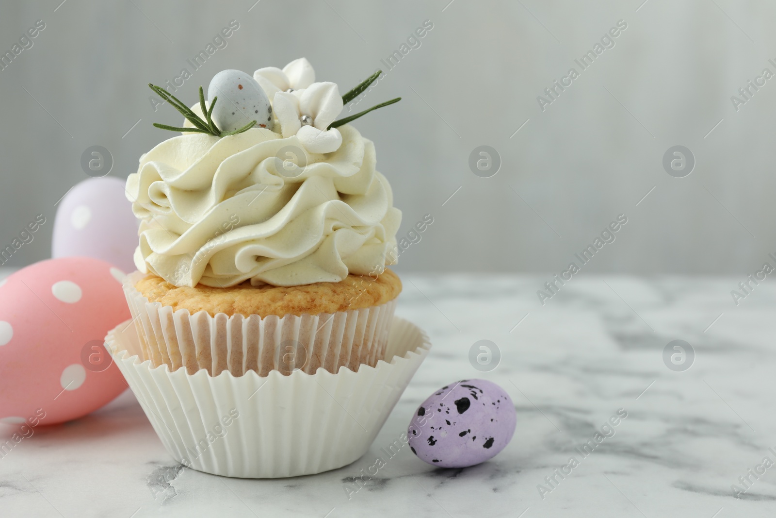 Photo of Tasty Easter cupcake with vanilla cream and eggs on white marble table, space for text