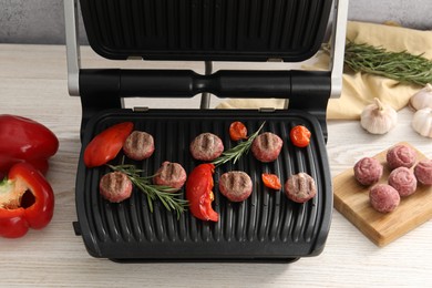 Photo of Electric grill with vegetables, meat balls and rosemary on wooden table