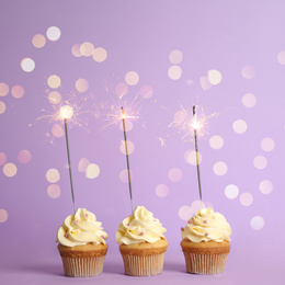 Image of Birthday cupcakes with sparklers on violet background