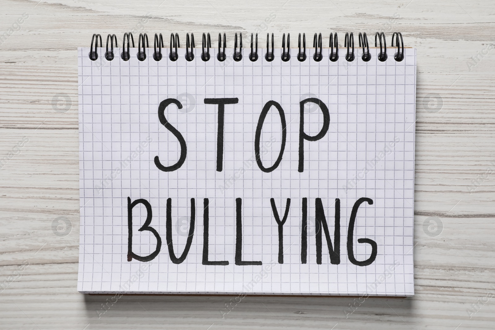 Photo of Text Stop Bullying written in notebook on white wooden table, top view