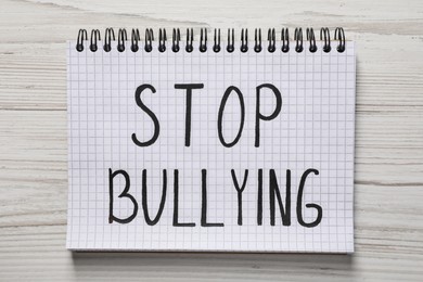 Photo of Text Stop Bullying written in notebook on white wooden table, top view