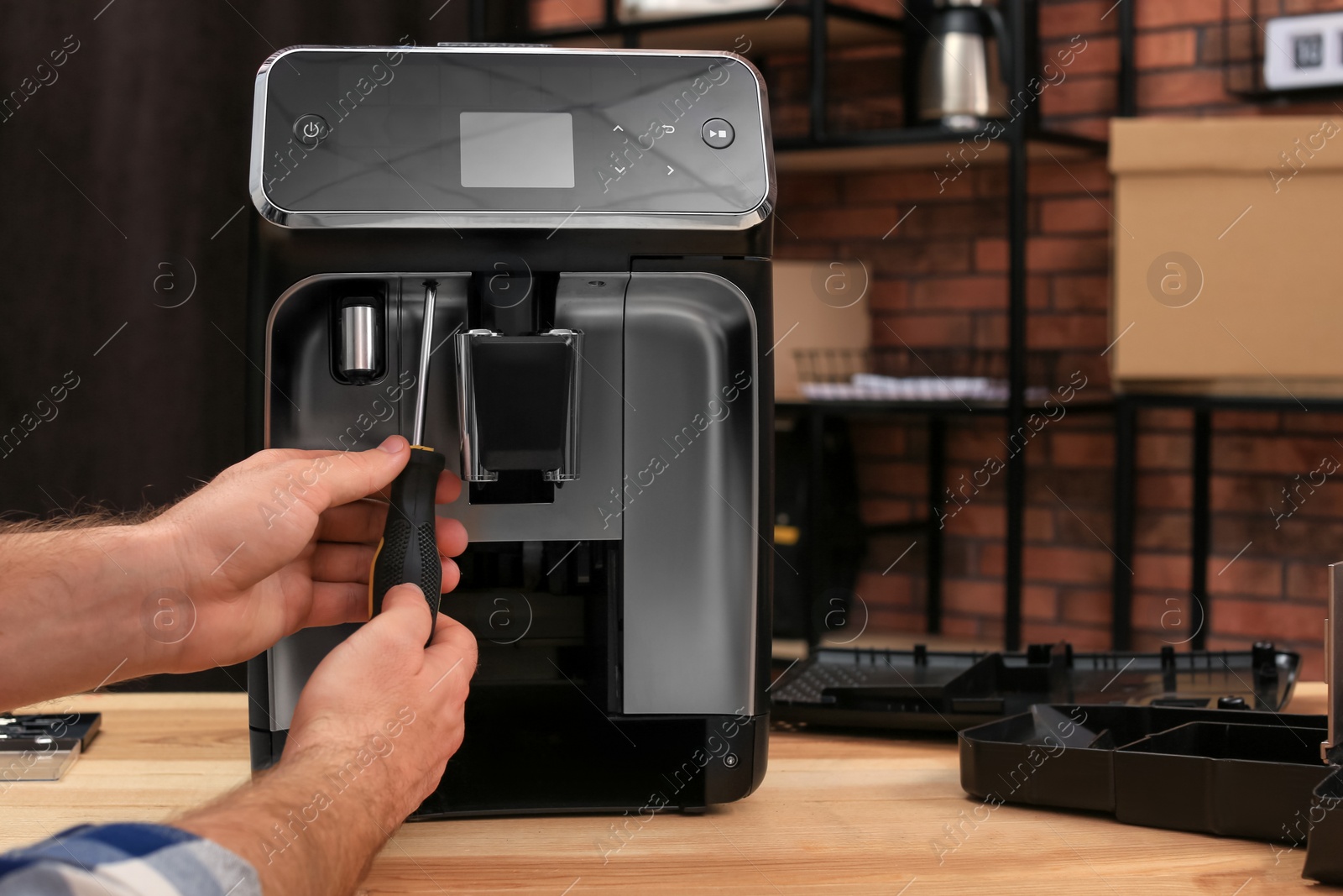 Photo of Man with screwdriver fixing coffee machine at table indoors, closeup