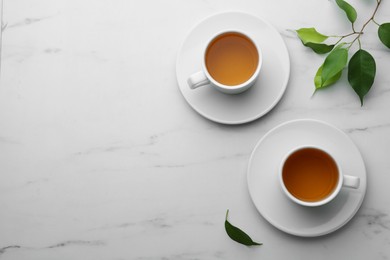 Green tea in cups with leaves on white marble table, flat lay. Space for text